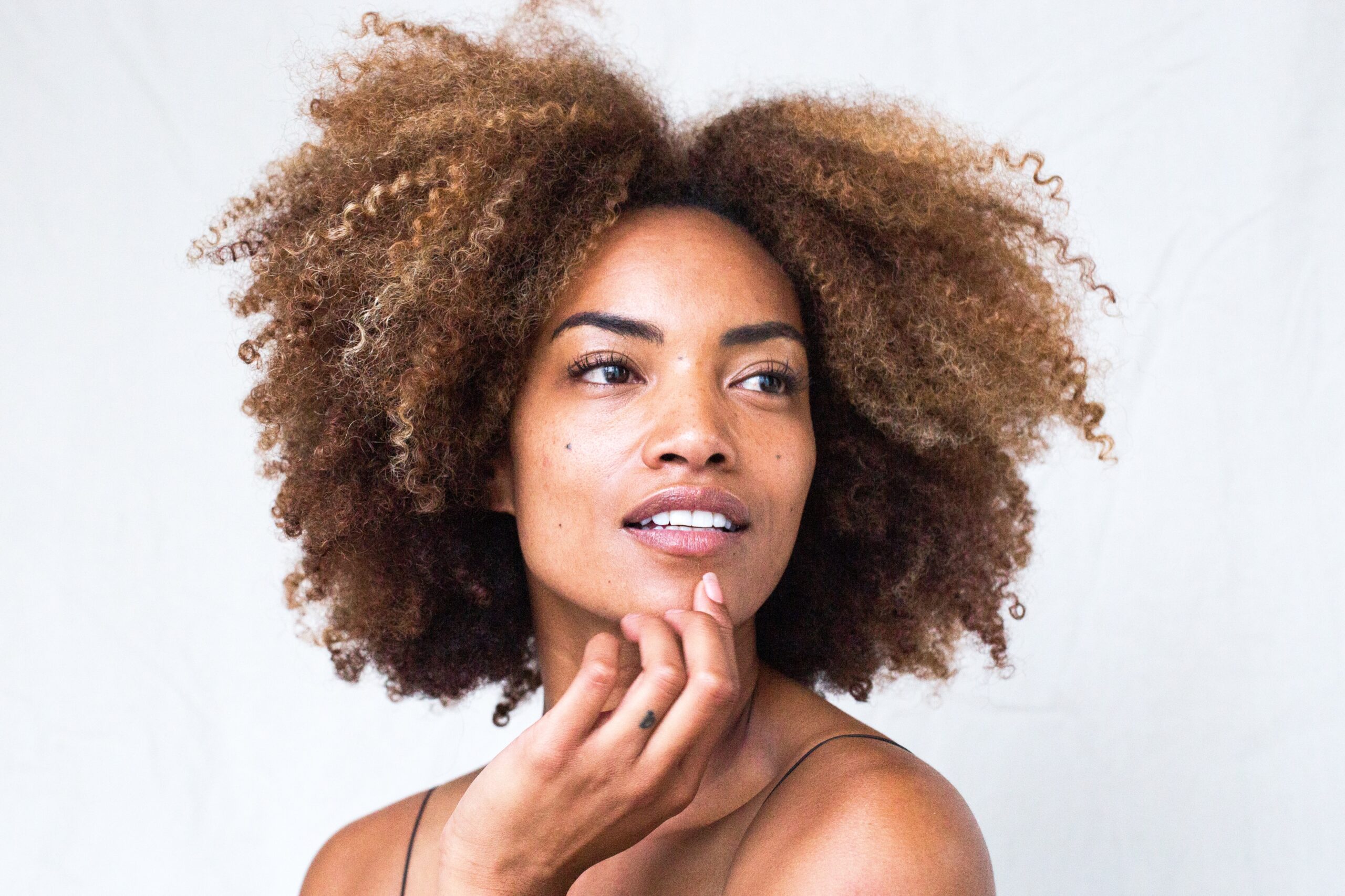 Smiling woman with natural curly hair touching her face, showcasing radiant skin