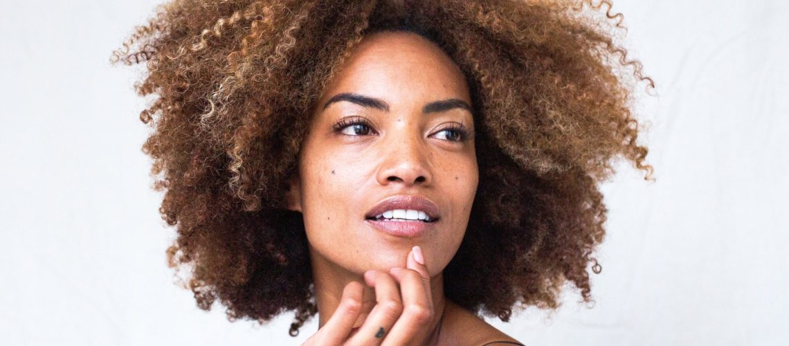 Smiling woman with natural curly hair touching her face, showcasing radiant skin